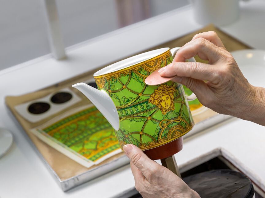 Porcelain decoration: A person is carefully applying a colored design by hand to a white teapot.