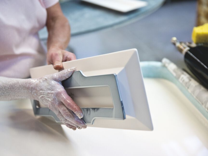An employee carefully removes a freshly cast rectangular porcelain piece from a mould.