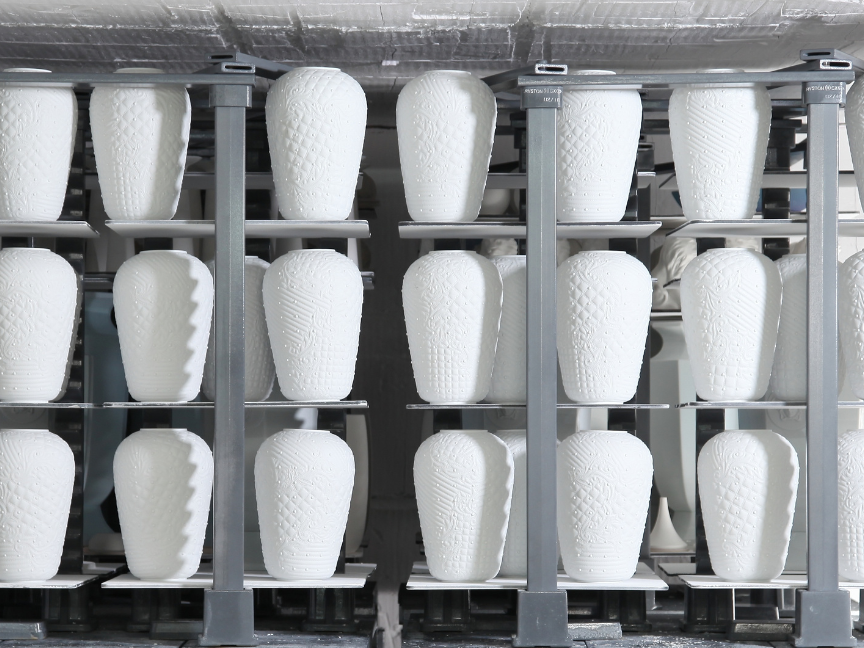 Porcelain manufacturing: White, unfired vases stand in rows on an industrial conveyor rack in a production facility.