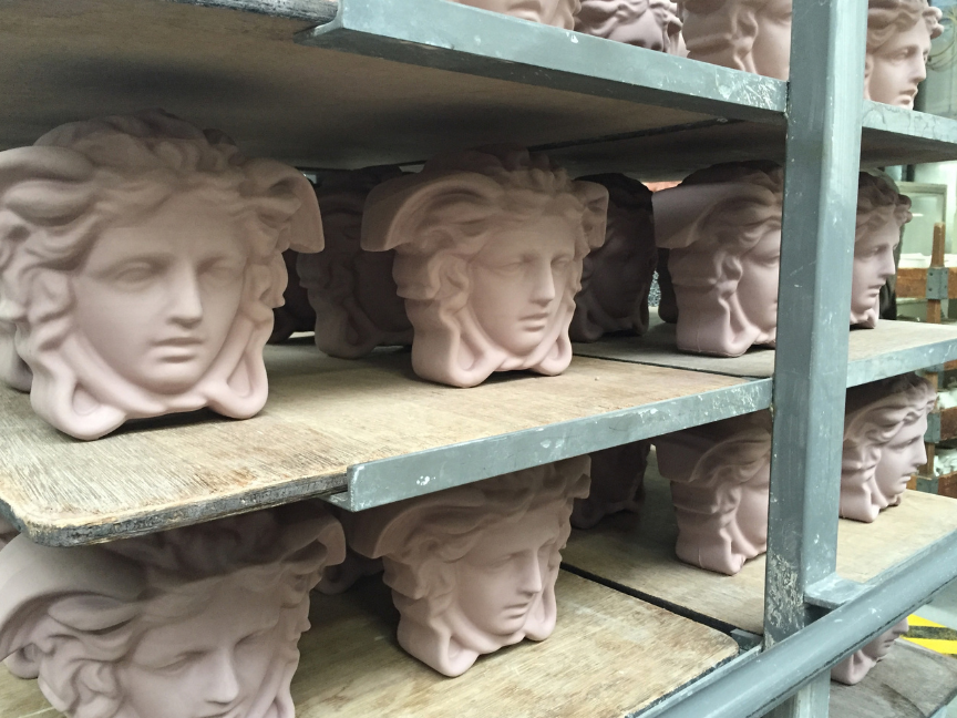 Unfired, pink &ldquo;Versace Medusa&rdquo; sculpture heads are stored on wooden shelves in a workshop prior to firing.