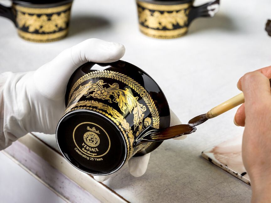 A black cup with gold decorations is glazed and finished by hand using a brush.